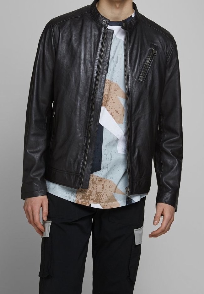 Giubbotto in pelle nera da motociclista con colletto rotondo, tasca con zip e texture liscia, indossato sopra una camicia a fantasia e pantaloni cargo.