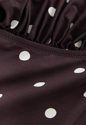 Brunt stof med hvide prikker; har samlet tekstur langs kanten og pæn syning. Glat, blød tekstur.