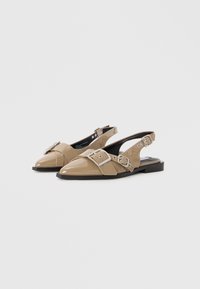 Beige patent leather slingback shoes with a pointed toe, featuring two decorative silver buckles and a low black heel.
