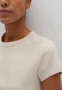 T-shirt beige a righe con scollo rotondo semplice e maniche corte, che mostra una texture morbida e sottili linee orizzontali.