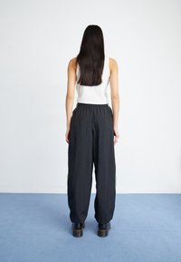 Pantalones anchos negros con rayas laterales verdes, combinados con una camiseta sin mangas blanca. Tejido suave, llevados con zapatos de plataforma gruesos negros.