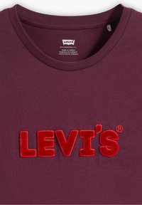 Mörkröd t-shirt med röd sammet broderad "LEVI'S" logga centrerad under kragen, etikett inuti visar att den är tillverkad i Turkiet, Levi's märke.