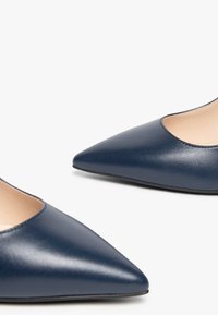 Ballerines en cuir bleu marine à bout pointu avec un design épuré, texture lisse et côtés découpés, reposant sur un fond clair.