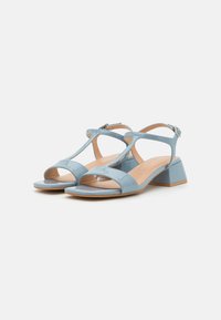 Sandali con tacco in vernice blu, design a T-strap, punta aperta e tacco a blocco. La soletta è beige con una superficie liscia.
