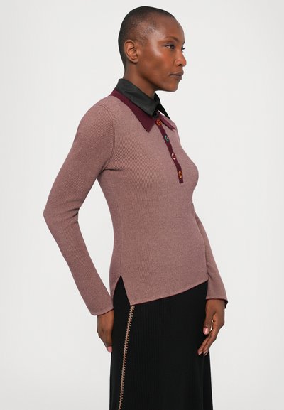 Woman with short hair wearing a mauve ribbed long-sleeve top with a dark maroon collar and black ribbed skirt with side stitching.