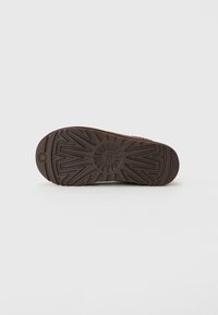 Brown rubber sole of a shoe with patterned tread and a small circular logo near the heel, photographed on a white background.