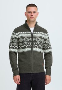 Grön stickad cardigans med dragkedja, som har ett mönstrat mönster i vitt och mörkgrönt samt ribbade mudd och nederkant.