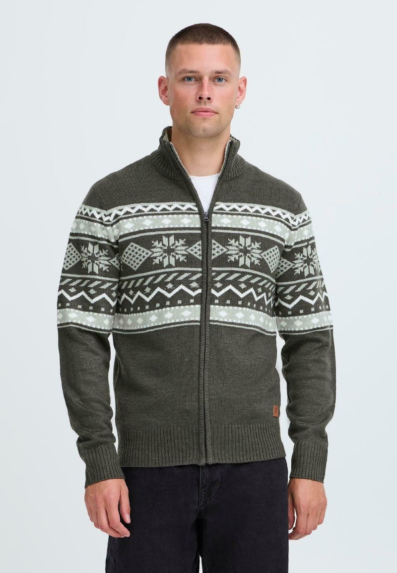 Grön stickad cardigans med dragkedja, som har ett mönstrat mönster i vitt och mörkgrönt samt ribbade mudd och nederkant.
