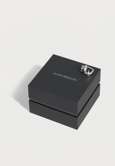 Μαύρο τετράγωνο κουτί κοσμημάτων με το λογότυπο "ALAN CROETTI" και ένα ασημένιο δαχτυλίδι σε σχήμα κορώνας που ξεκουράζεται στην κορυφή, σε λευκό φόντο.