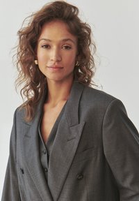 Grijze dubbelzijdige blazer met gesneden revers, gecombineerd met een bijpassend vest. Bevat textuurstof en subtiele zwarte knopen.