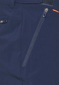 En närbild av marinblått tyg med två dragkedjefickor, en vertikal och en horisontell, med mörkblå dragkedjehandtag och en liten orange accent.