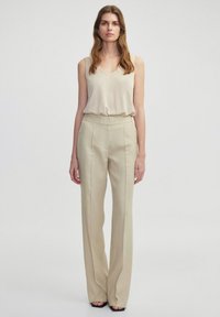 Beige mouwloos topje met een v-hals, gecombineerd met hoge taille, wijde broek in een gestructureerde, lichtbeige stof. Zwarte hakken.