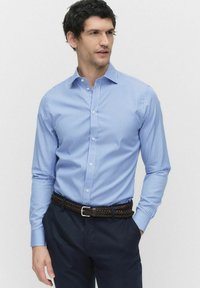 Lichtblauw gestreept overhemd met een puntkraag, lange mouwen en witte knopen, gecombineerd met donker marineblauwe broek en een gevlochten bruine riem.