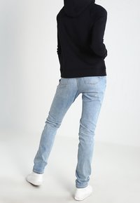 Ljusblå jeans och en svart hoodie med en avslappnad passform, synliga sömmar och en känguruficka. Bärs med vita sneakers.