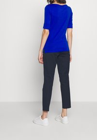 Blå långärmad topp i kombination med mörka byxor, med en figurnära design och sidofickor, kompletterad med vita sneakers.