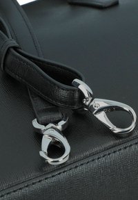 Schwarze Handtasche mit strukturiertem Äußeren, zwei Metallclips und glatten Ledertrageriemen. Auffällige, glänzende silberne Hardwareakzente.