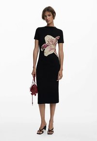 Mustast lühikeste varrukatega midi pikkusega kleit, millel on suur valge ja roosa lillemuster. Modell hoiab punast käekotti ja kannab musti sandaale.