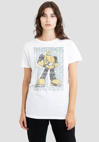 White cotton t-shirt featuring a graphic of a yellow robot with black accents, accompanied by "Transformers" text and "More Than Meets the Eye."