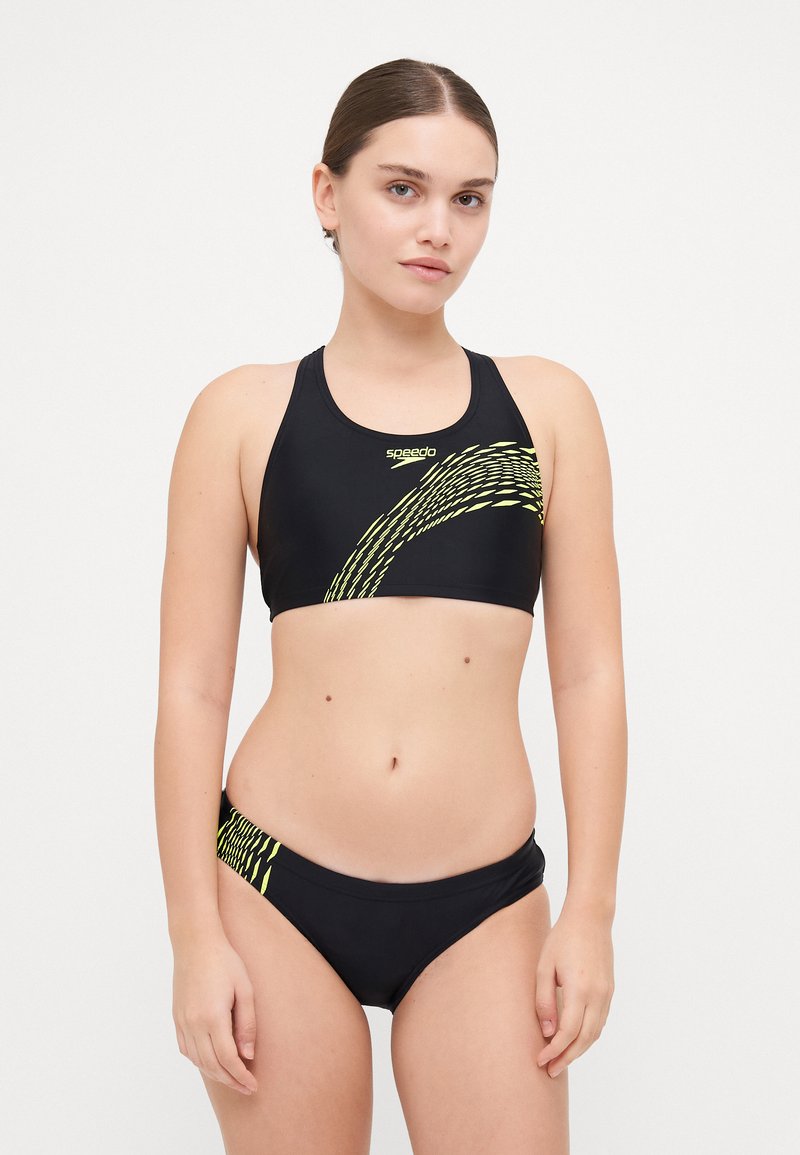 Svart bikini-sett med en høyhalset topp og matchende underdeler. Har et gult bølgedesign og Speedo-logo. Glatt tekstur.