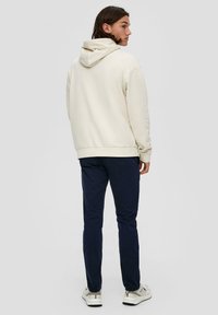 Lichtbeige hoodie met een geribde zoom en capuchon, gecombineerd met navy slim-fit broek. De outfit is afgewerkt met witte sneakers en heeft een gladde textuur.