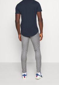 Námořnické tričko s krátkým rukávem, šedé kostkované kalhoty a bílé tenisky s modrými a červenými akcenty, viděno zezadu.