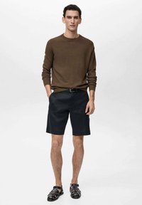 Brauner Strickpullover, schwarze Shorts und schwarze Sandalen. Das Outfit ist lässig und weist eine entspannte Silhouette mit einer glatten Textur auf.
