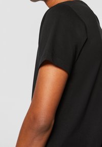 Černé bavlněné tričko s krátkými rukávy, kulatým výstřihem a hladkou texturou, z pohledu z boku.