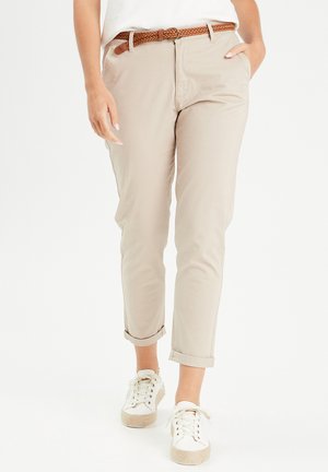 Beige Chinos mit umgeschlagenen Bündchen, ausgestattet mit seitlichen Taschen und einem braunen geflochtenen Gürtel, kombiniert mit weißen Sneakers mit strukturierten Sohlen.