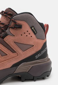 Brune og grå turstøvler med semsket skinn, mesh og gummi-materialer. Merkbar GORE-TEX merkevare og avansert chassiskonstruksjon for støtte.