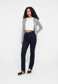 Jeans azul oscuro con un corte recto, combinados con un top blanco cortado y un cárdigan gris claro con cremallera. Zapatillas negras con detalles en blanco.