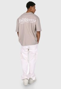 Grå oversized t-shirt med hvid grafik på ryggen, kombineret med hvide cargo bukser og hvide sneakers, set bagfra.