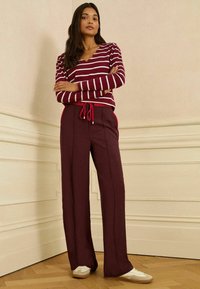 Burgundské kalhoty s širokými nohavicemi a červenými akcenty, se šňůrkou v pase, v kombinaci s dlouhým rukávem pruhovaným v maroon a bílé barvě. Hladká textura, neformální design.