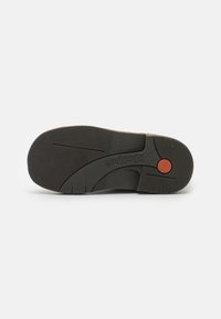 Semelle en caoutchouc noir avec surface texturée ; présente un accent circulaire rouge et des lignes courbes pour plus de flexibilité.