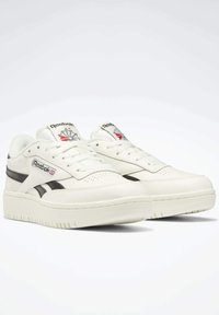 White leather sneakers with black side stripes, padded collar, and lace-up design. Features Reebok logo and red maple leaf detail.