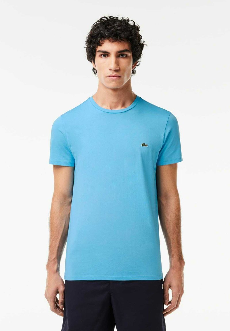 Camiseta de algodón azul clara con cuello redondo, mangas cortas y pequeño logo bordado en el pecho. Textura suave, ajuste clásico.