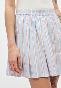 Jupe plissée bleu clair avec des rayures verticales en corail et blanc. Taille élastique et texture de tissu lisse et brillante.