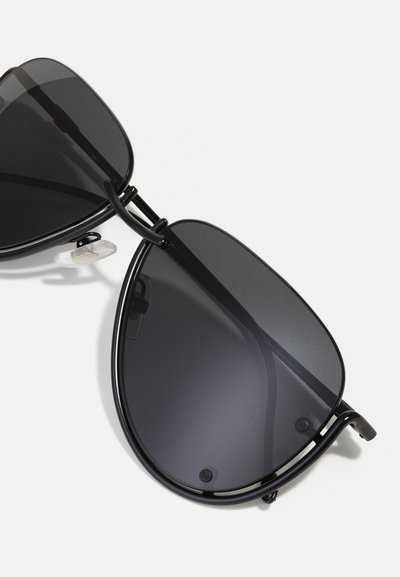 Lunettes de soleil aviateur noires avec des verres teintés, monture en métal et plaquettes de nez transparentes. La forme des verres est en goutte d'eau, avec des détails matériels minimaux.