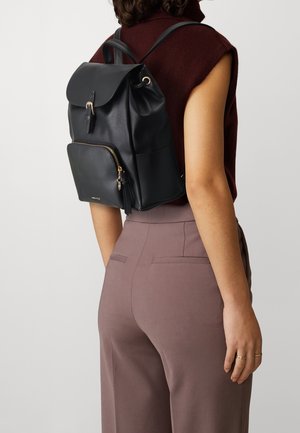 Schwarzer Leder-Rucksack mit einem umklappbaren Deckel, vorderer Reißverschlusstasche, Akzenten aus goldenem Metall und verstellbaren Schulterriemen. Glatte Textur.