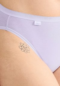 Jasnofioletowe bawełniane majtki typu hipster z delikatnym koronkowym wykończeniem w pasie, z małą metką logo. W pobliżu widoczny jest tatuaż w kształcie kwiatu.