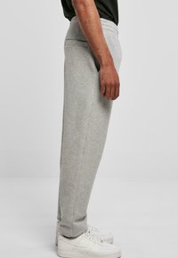 Szare spodnie dresowe z elastycznym pasem, bocznymi kieszeniami i zwężanym krojem. Tkanina ma miękką fakturę. Noszone z białymi trampkami.