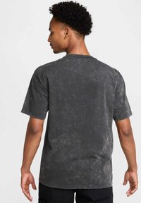 T-shirt nera a maniche corte con una texture sbiadita e lavata. Collo rotondo e vestibilità rilassata. Vista posteriore che mostra una superficie di tessuto liscia e senza grafiche.