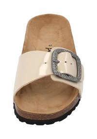 Beige slip-on sandal with a glossy upper, large metal buckle, and a textured cork sole. Interior features a soft, natural finish.