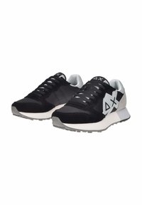Sneaker neri e grigi caratterizzati da una combinazione di materiali tessili e scamosciati, superficie liscia, logo bianco prominente e suola in gomma resistente.