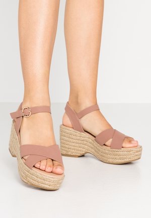 Sandales compensées à plateforme rose avec brides croisées, semelle en jute tissé et détail boucle dorée sur la bride de la cheville.