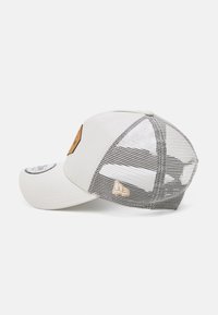 Balta kepurė su tinkliniu užpakaliu, su tekstūruota ruda odos etikete ir mažu logotipu. Iškraipytas bill ir reguliuojamas snapback dizainas.
