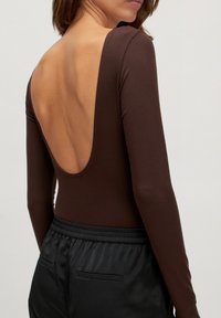 Bruine lange mouwen bodysuit met een diepe ruguitsnijding, gecombineerd met zwarte high-waisted broek met een gladde textuur en elastische tailleband.