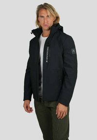 Veste isolante noire avec fermeture éclair sur le devant, capuche et détail de logo sur la manche. Comprend des poches latérales et une texture lisse et élégante.