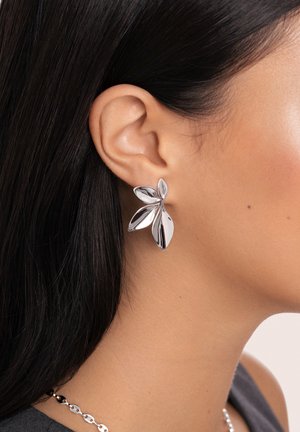Zilverkleurige oorbellen in de vorm van bloemen met gepolijste, reflecterende oppervlakken, met gelaagde bloemblaadjesontwerpen die zijn bevestigd aan een stud-achterkant.