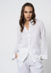 Camicia button-up bianca in lino con maniche lunghe, caratterizzata da una vestibilità rilassata, una trama sottile e bottoni perlacei lungo la parte anteriore.