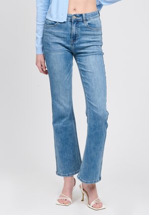 Jeans a zampa di colore azzurro chiaro in denim; presentano una vita a metà altezza, tasche frontali e un leggero effetto sbiadito. Abbinati a sandali bianchi con cinturini.